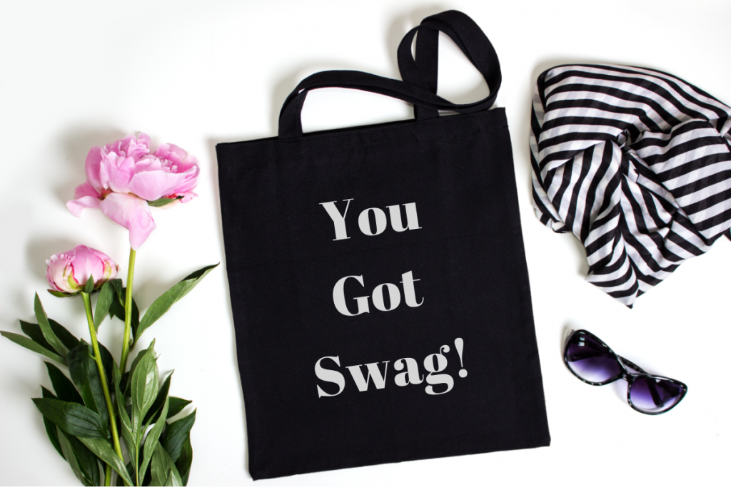 Company Swag - Image from Canva of a black canvas tote that says "you got swag!' on it, next to a scarf and sunglasses and a stem of peonies